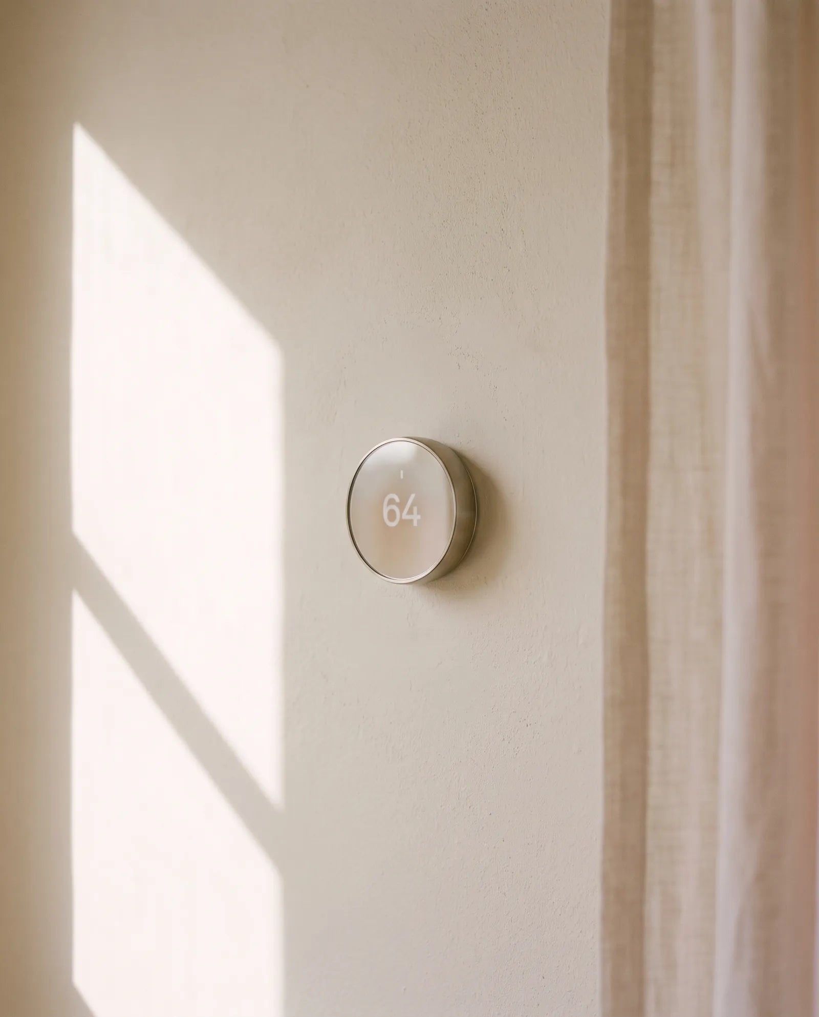 Wall thermostat set to 64 degrees in soft afternoon light